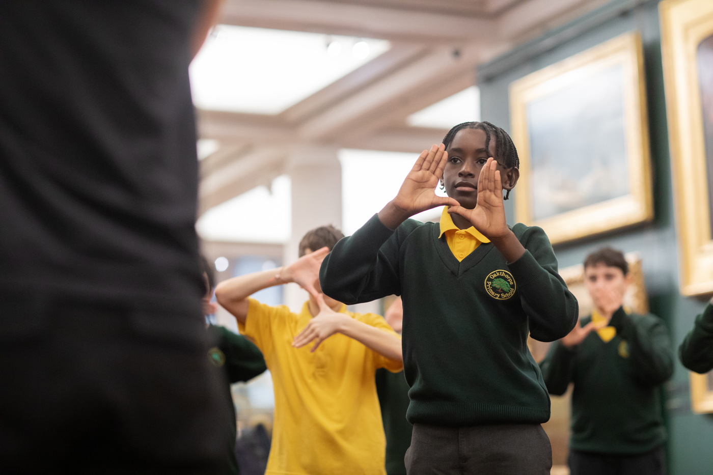 A group of students in uniforms with green tops are engaged in an activity inside a museum or gallery, with one student visibly focused and participating.