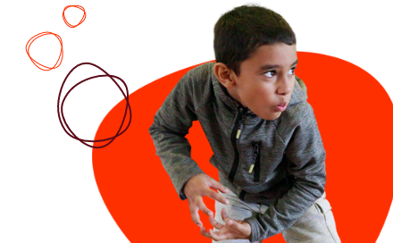 A boy wearing a gray jacket appears to be playing or mimicking a motion. The background is a bright red shape with three outlined circles on the left side.