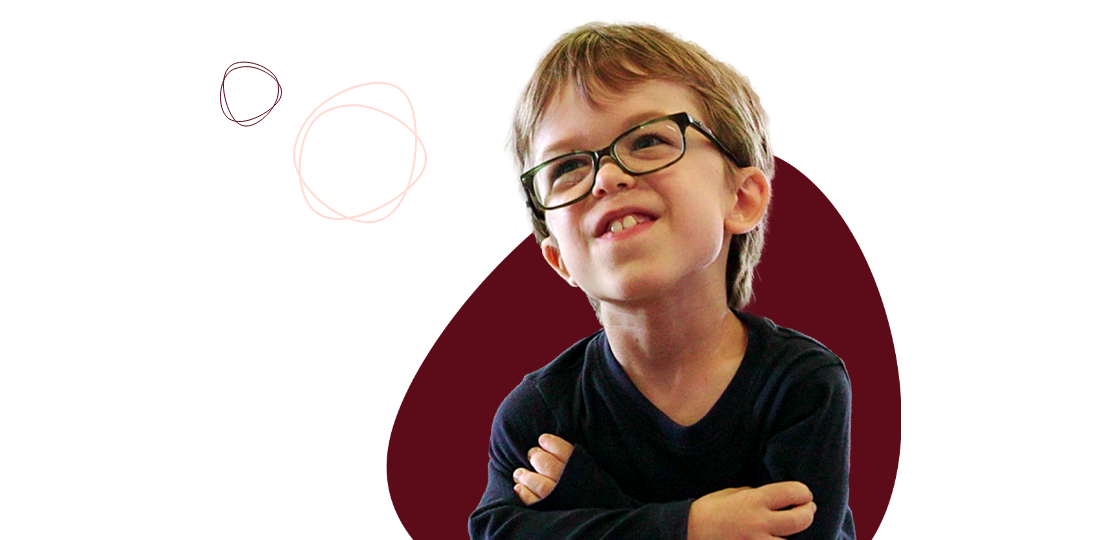 A young boy with glasses and crossed arms smiles while looking upwards, against a black background with maroon and white doodles.