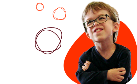 A young child with glasses and short hair wears a dark shirt and smiles, arms crossed, in front of a black and orange background with drawn circles.