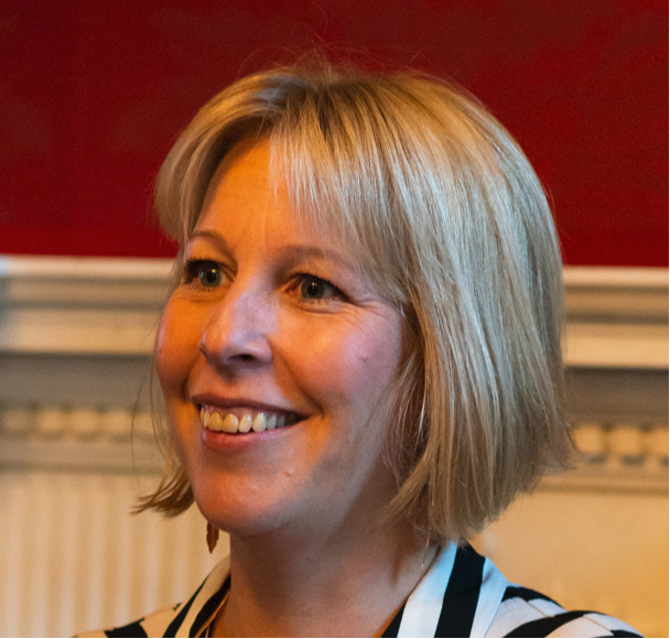 A woman with blonde hair and a striped shirt smiles while looking slightly to the side.