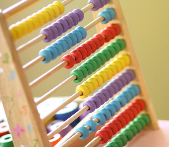 A colorful wooden abacus with rows of blue, yellow, green, and red beads against a soft-focus background.