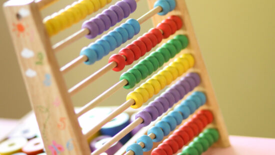 A colorful wooden abacus with rows of blue, yellow, green, and red beads against a soft-focus background.