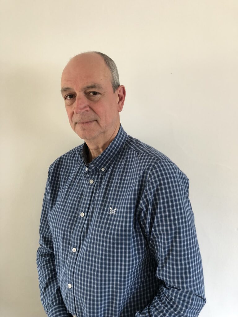 A middle-aged man with a receding hairline wearing a blue checkered shirt, standing against a plain white background.