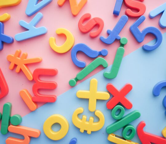 Plastic multicolored letters and symbols are scattered on a pink and blue background.