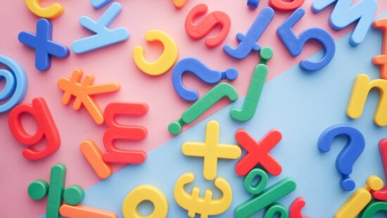 Plastic multicolored letters and symbols are scattered on a pink and blue background.