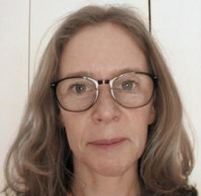 A woman with glasses and shoulder-length hair looks directly at the camera against a plain background.