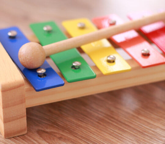 A colorful wooden xylophone with eight metal bars in different colors and a wooden mallet resting on it.