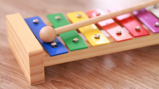 A colorful wooden xylophone with eight metal bars in different colors and a wooden mallet resting on it.