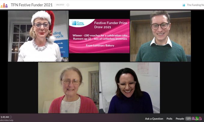 A video call screenshot shows four people smiling. The top-left participant wears a Santa hat. Text on the screen includes "TFN Festive Funder 2021," and details of a prize draw for "Festive Funder Prize Draw 2021.