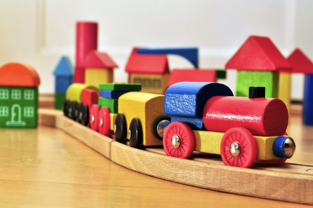 Close-up of a colorful wooden toy train on a wooden track, surrounded by various wooden toy buildings.